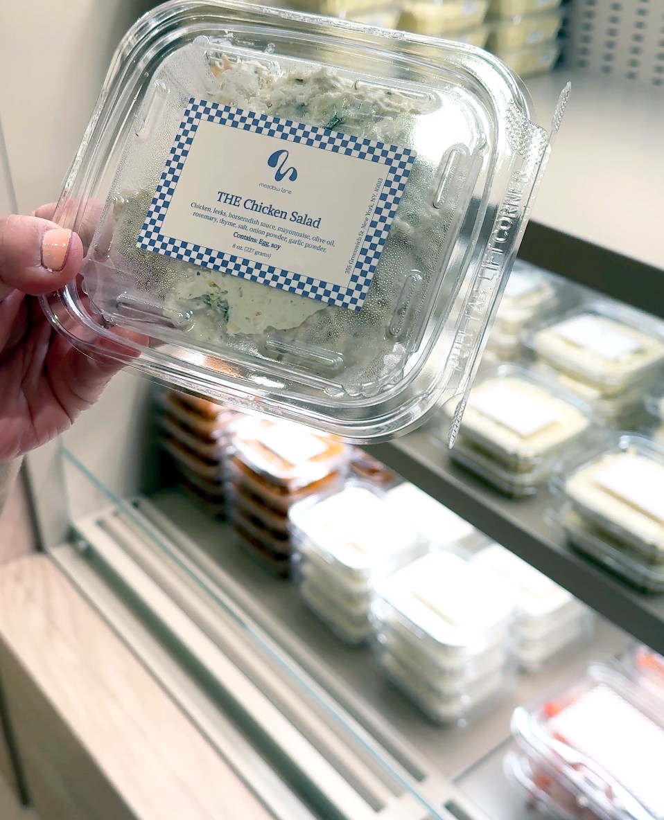 Someone holding up a container with chicken salad at a grocery store.